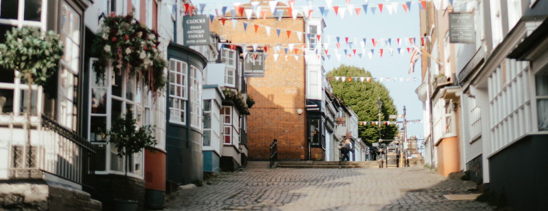 Photo of a cobbled street with shops and houses either side and red, white and blue bunting going across